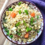 cauliflower fired rice in bowl with peas and carrots garnish on top