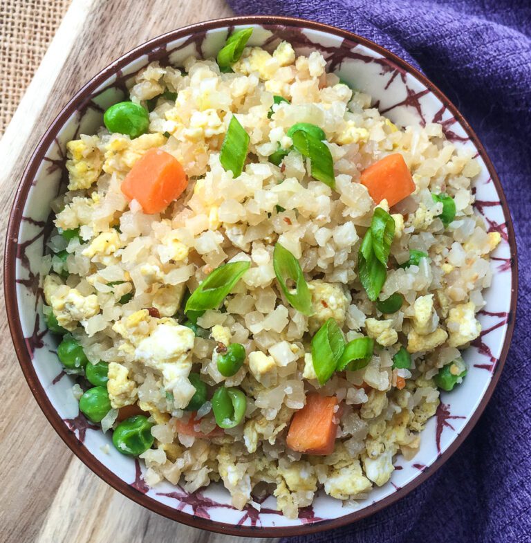 cauliflower fired rice in bowl with peas and carrots garnish on top
