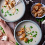low histamine creamy cauliflower soup in 2 serving bowls garnished with gluten free croutons and parsley