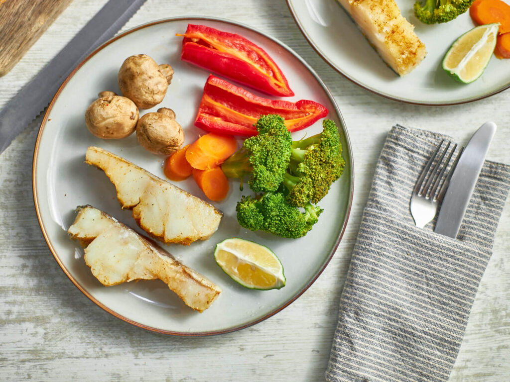 steamed cod with vegetables on a white plate